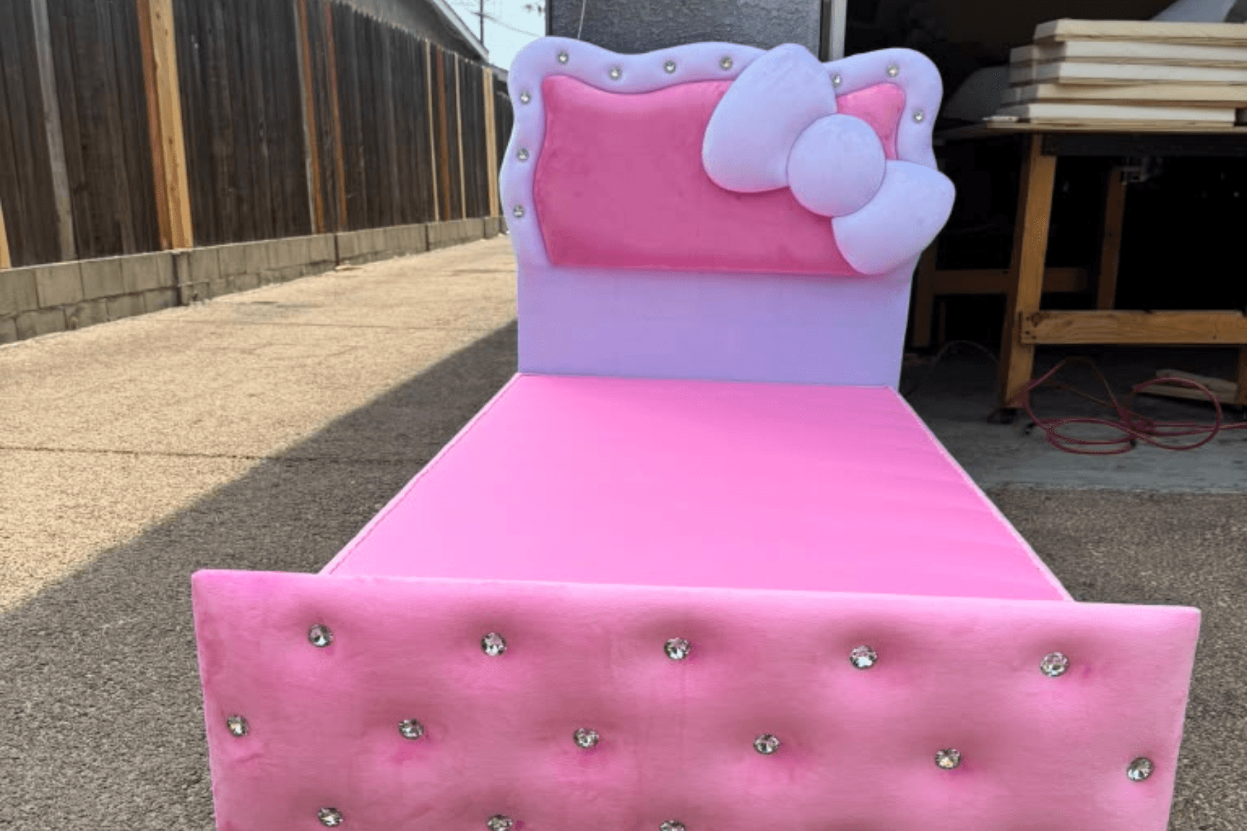 Pink velvet bed with a white bow headboard and a crystal-button tufted footboard, outside the workshop roller door